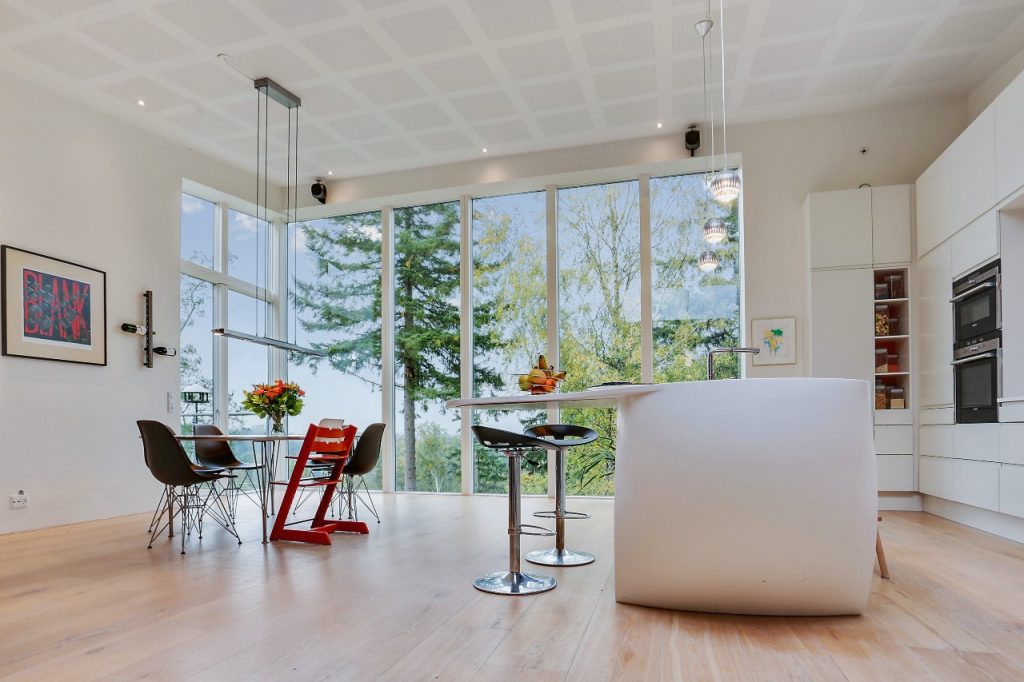 Køkken med kogeø med barstole, lyse materialer og vindue fra gulv til loft. Stue og køkken adskilles af lille trætrappe og oppudset designbeton i arkitekttegnet lavenergihus. Design fra Bozel - når typehuse ikke altid er nok